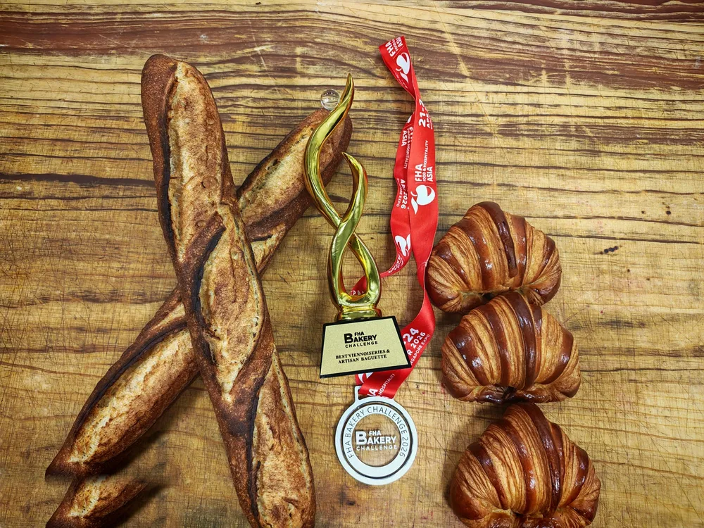 FHA Bakery Challenge 2026 trophy and medal for Best Viennoiseries & Artisan Baguette beside Chef Terry's sourdough baguettes and croissants